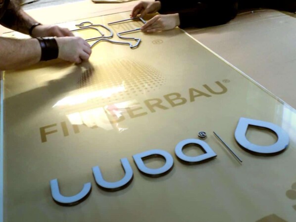 przyklejanie elementów reklamy na płycie pleksiglasu z użyciem wydrukowanego szablonu